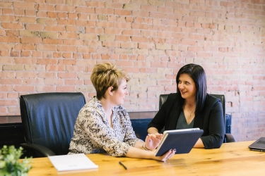 Dos mujeres profesionales conversando sobre temas financieros sentadas frente a un escritorio
